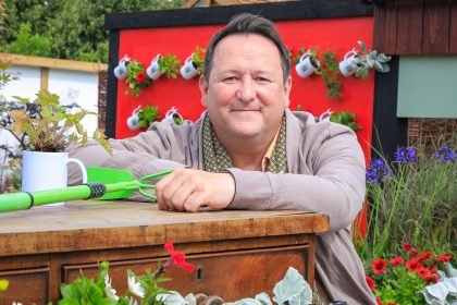 Photograph of Mark Lane leaning on an upcycled chest of drawers in the RHS-BBC Morning Live Budget-friendly Feature Garden at RHS Hampton Court Palace Garden Festival 2023, designed by Mark Lane from Mark Lane Designs Ltd